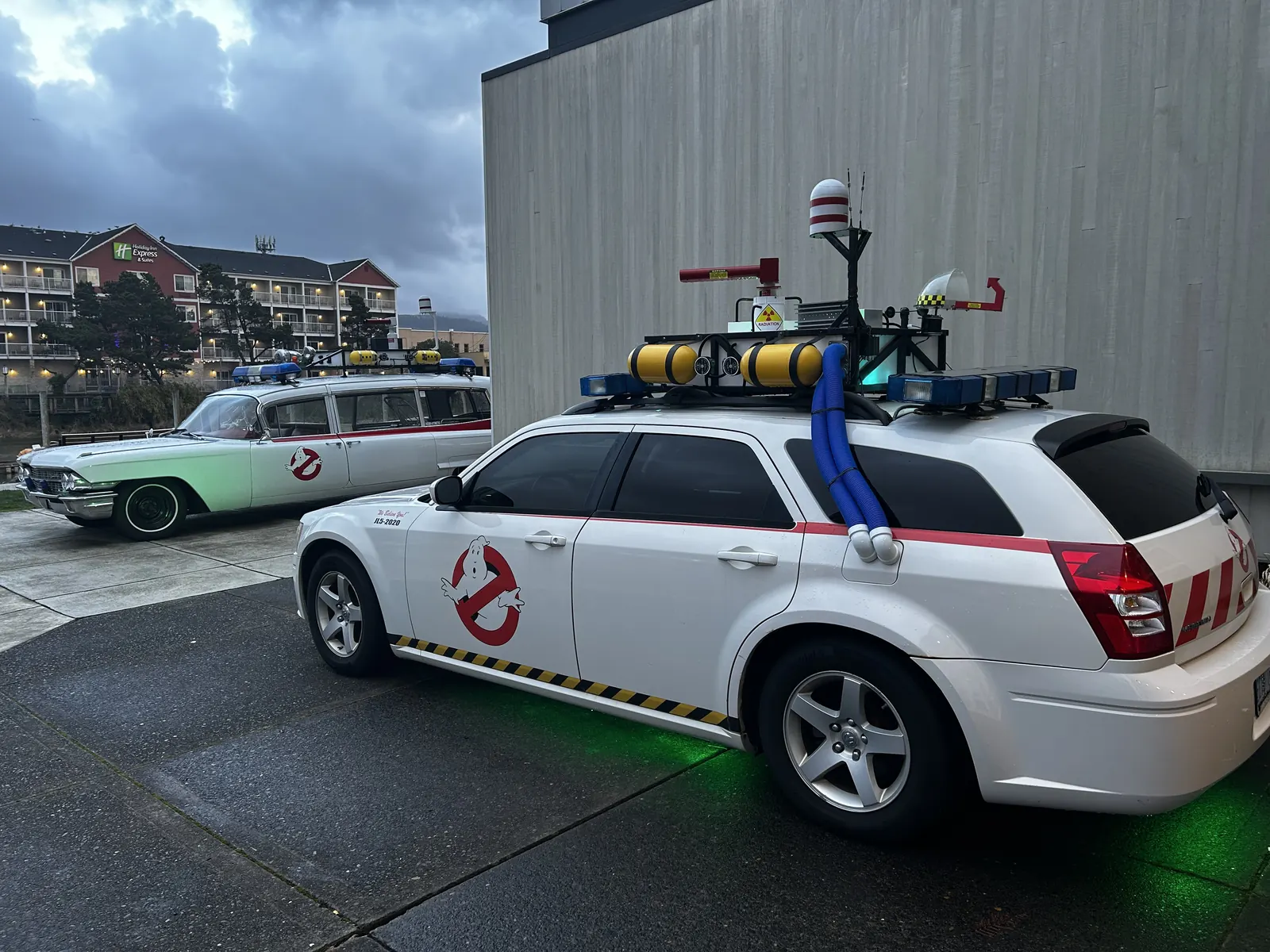 A ghost-hunting SUV glowing green at dusk beside the vintage Ecto wagon